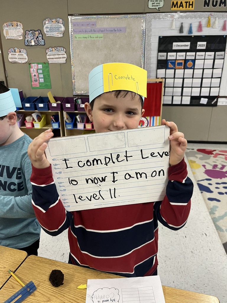  (Boy with 'Complete' crown): A young elementary school boy wearing a blue and yellow paper crown with the word "Complete" written on it. He is smiling and holding a dry-erase board that says, "I complet Level 10 now I am on level 11."  