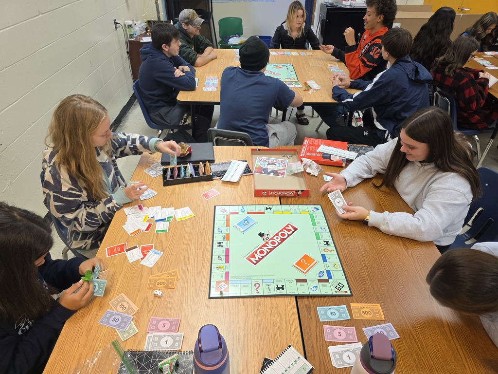 Group of students gathered around a Monopoly board, sorting money and cards while playing the game.