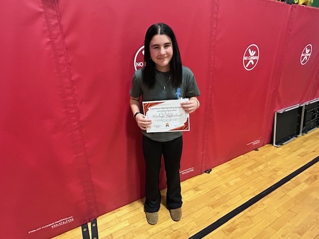 Student stands alone holding a certificate in front of red gym wall pads.