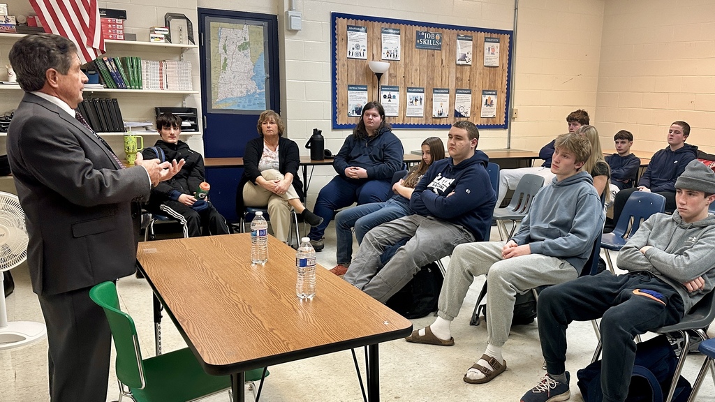 Senator Collamore addresses a Career Exploration class seated in rows, with classroom posters and bookshelves in the background.