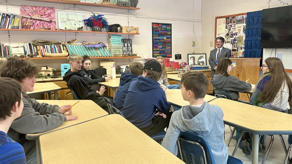 Senator Brian Collamore stands at the front of a classroom speaking to high school students seated at desks, listening attentively.