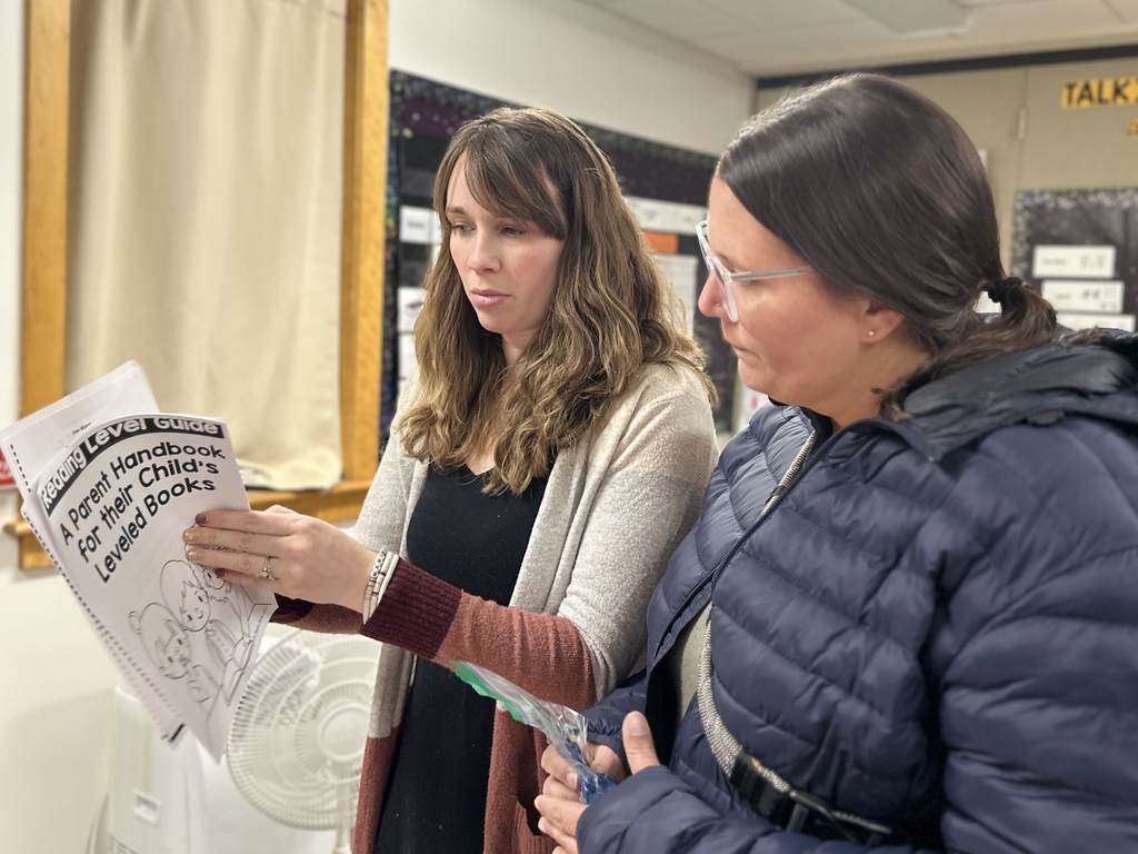 Two adults review a “Reading Level Guide” booklet together inside a classroom.