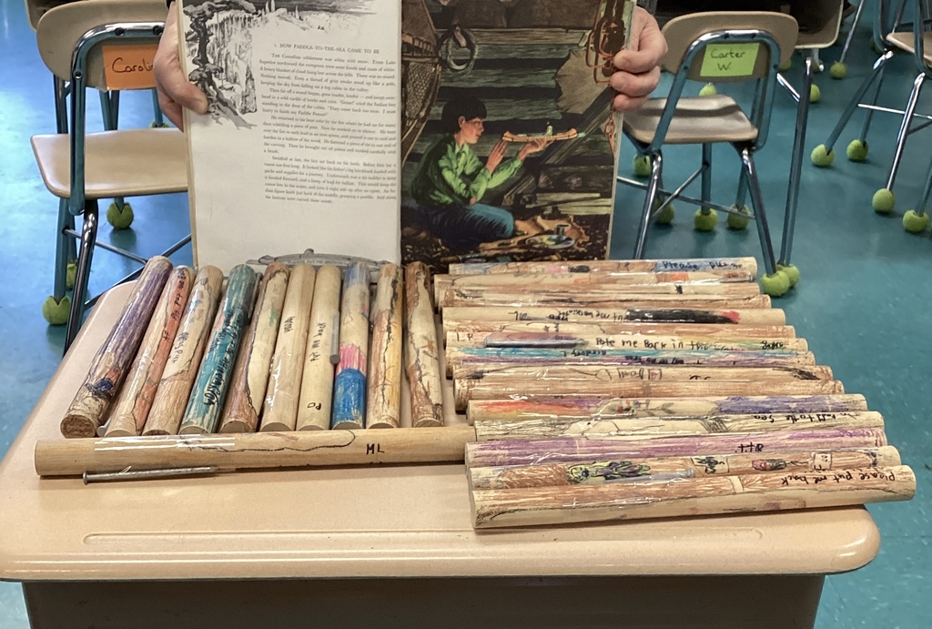 image of dowel canoes made by students in front of an open book.