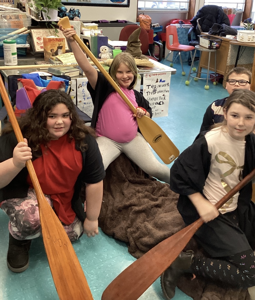 Three girls and one boy hold paddles in a classroom, one girl raising hers.
