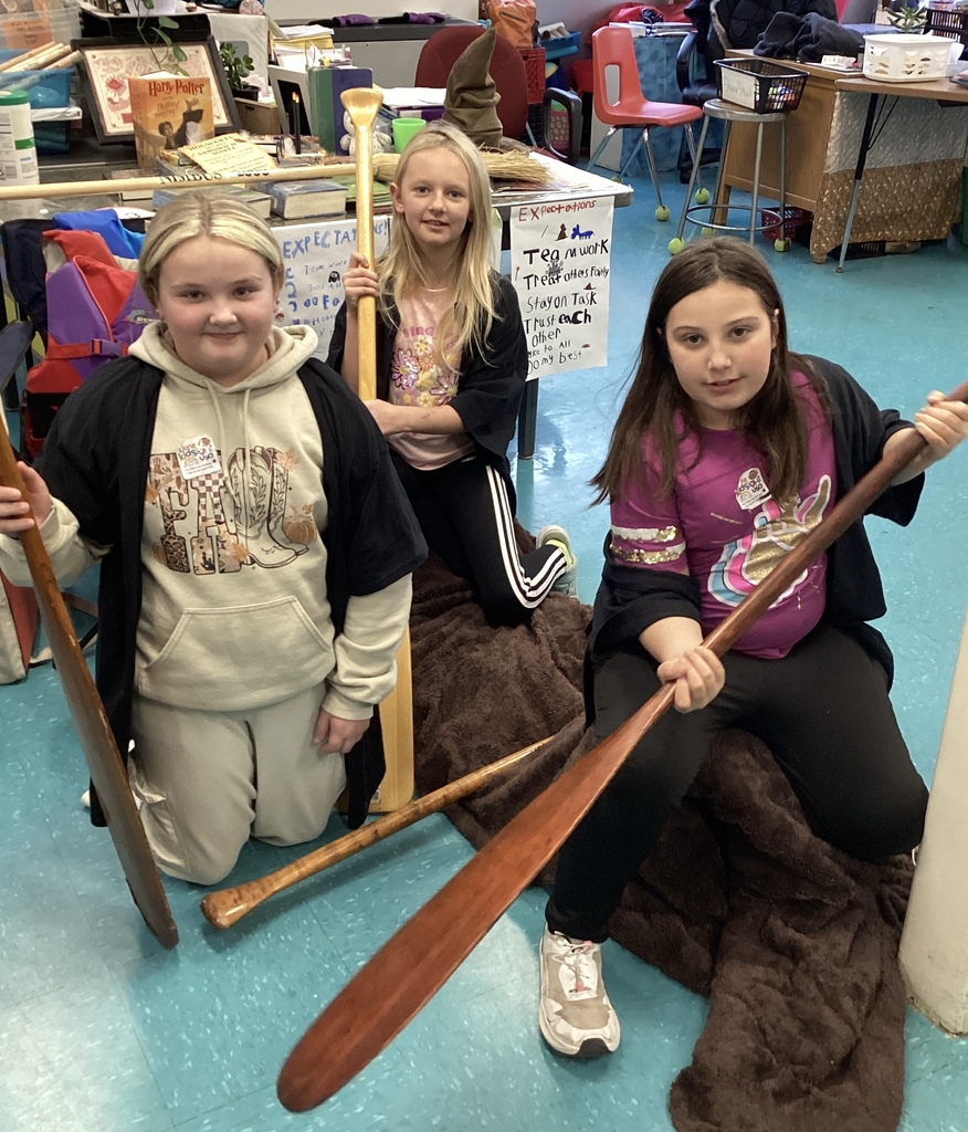 Three girls pose with paddles in a classroom.