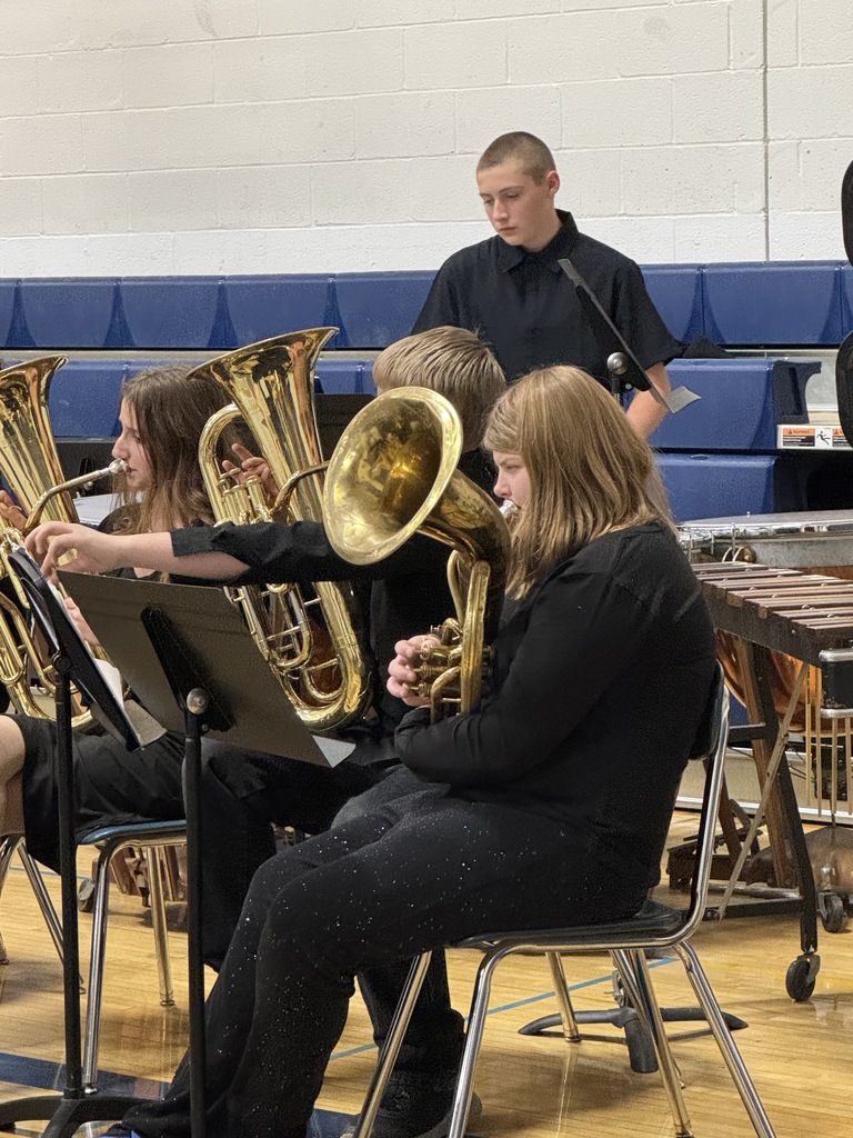Brass section students seated with tubas and euphoniums, following along with the conductor during the performance.
