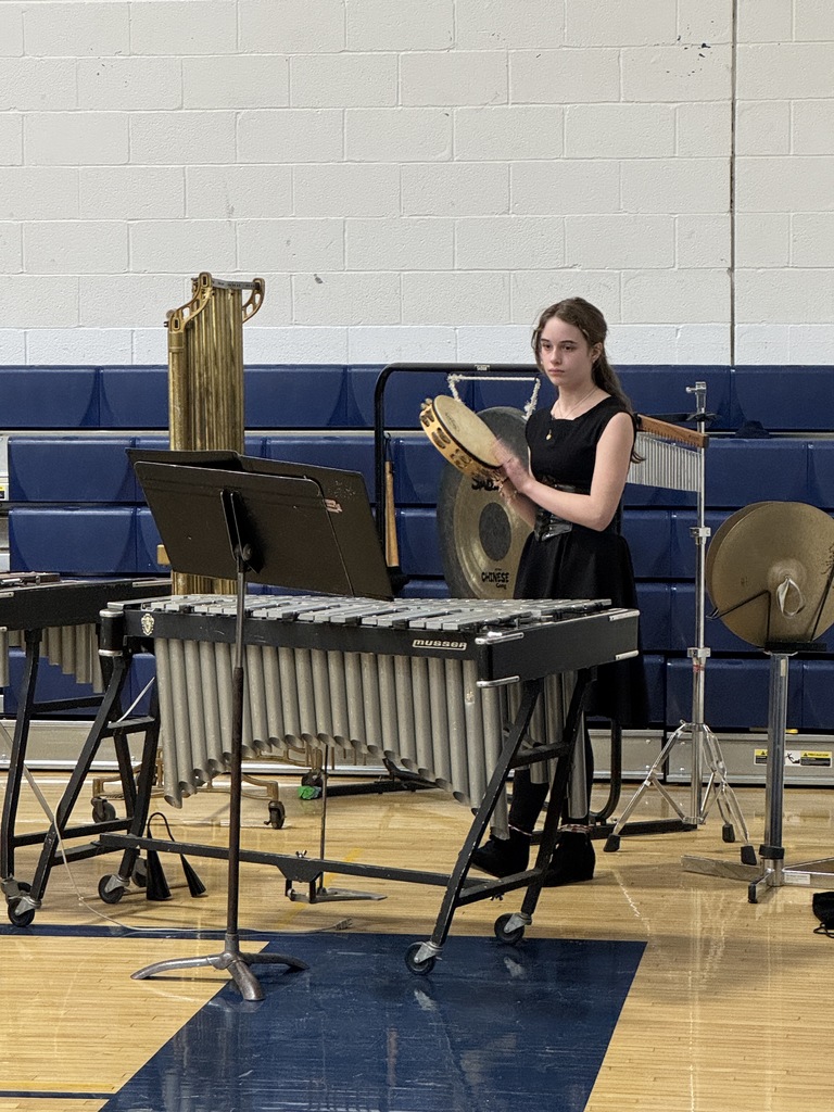 Student percussionist stands at a vibraphone and auxiliary percussion instruments, holding a tambourine during the concert.