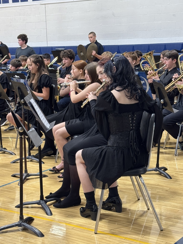 Close-up of student musicians playing flutes and brass instruments while seated in the band section.