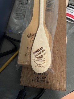 A wooden spoon engraved with “Chopped Champion” rests on a table as a cooking competition award.