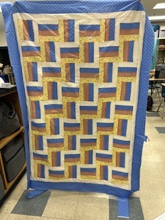 A handmade quilt with a geometric pattern is laid out flat, showing progress on a sewing project.