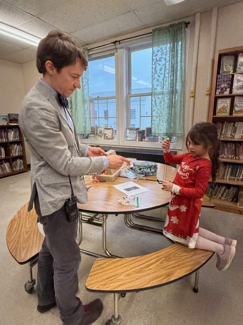 A teacher works one-on-one with a young student at a table during a classroom activity.