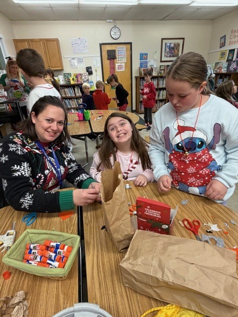 Students and a teacher smile while working on paper crafts at a classroom table.
