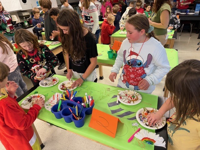 Several students gather around tables decorating paper plates with frosting and toppings.