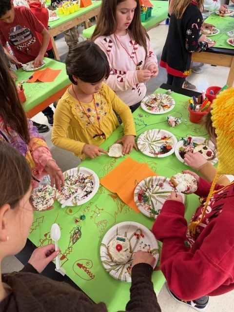 An overhead view of students decorating paper plate treats at a classroom table.