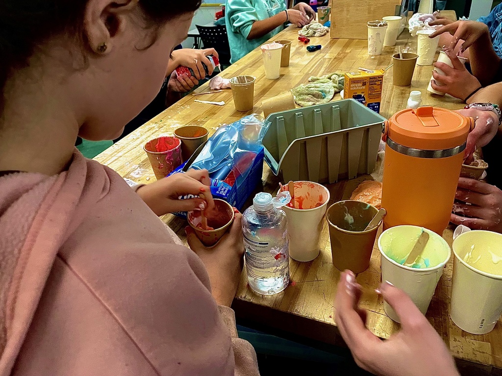 Students mix colorful slime ingredients in paper cups at a Design Lab worktable.