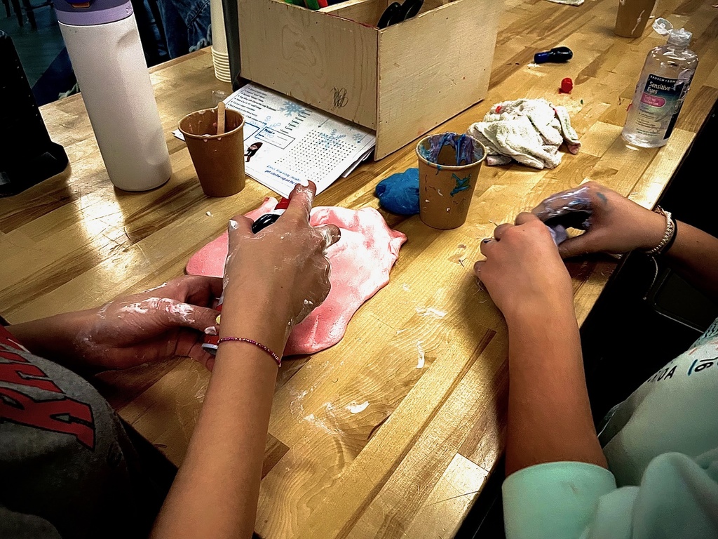 Two students knead pink and blue slime on a tabletop during a hands-on activity.