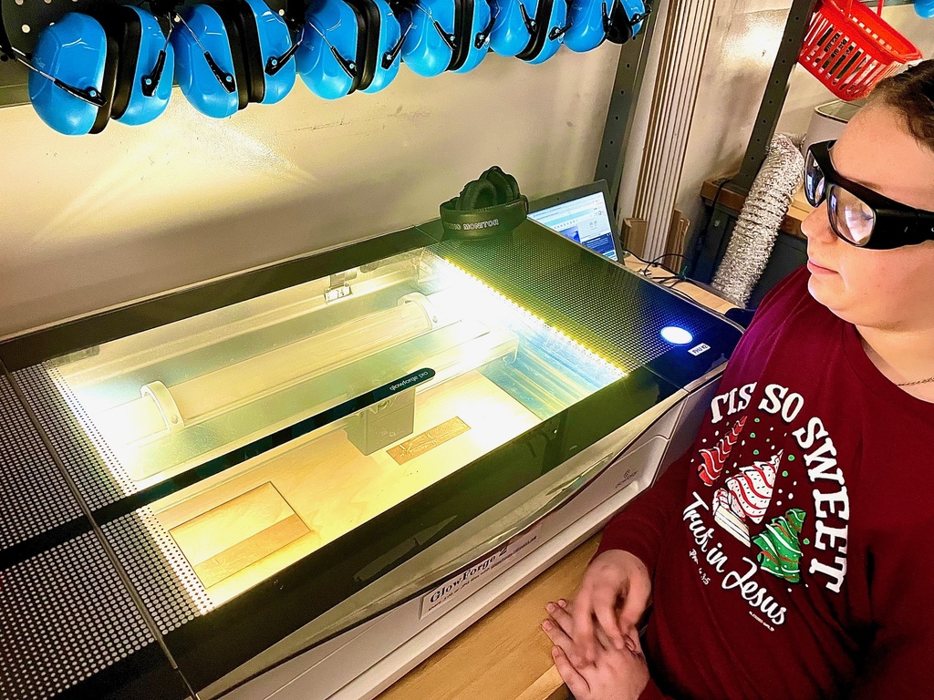 A student wearing safety glasses watches a laser cutter operate in the Design Lab.