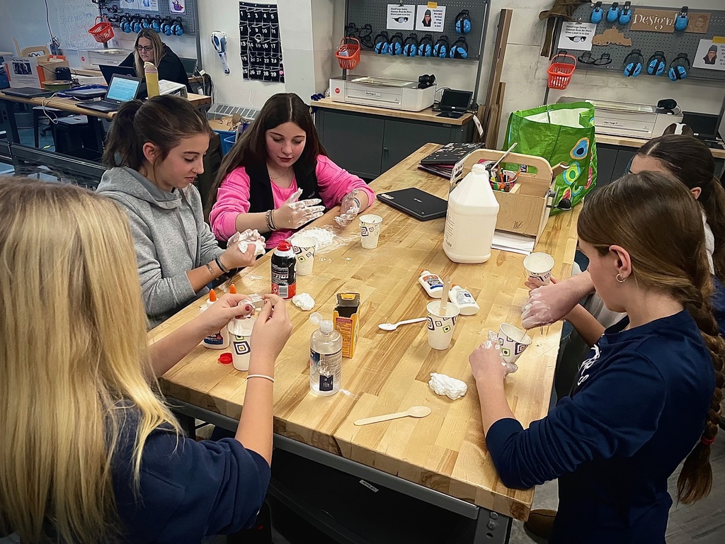 A group of students work together at a table mixing slime ingredients in paper cups.
