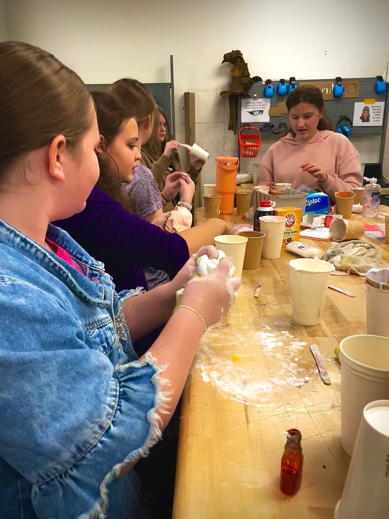 Students stand around a worktable mixing slime ingredients in cups during a Design Lab activity.