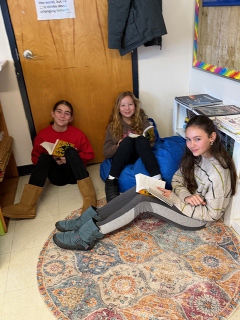Reading nook: Three students sit on the floor against a wall reading books during independent reading time.