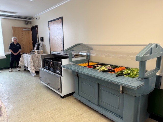 Empty salad bar station displays fresh vegetables including carrots, broccoli, and lettuce.