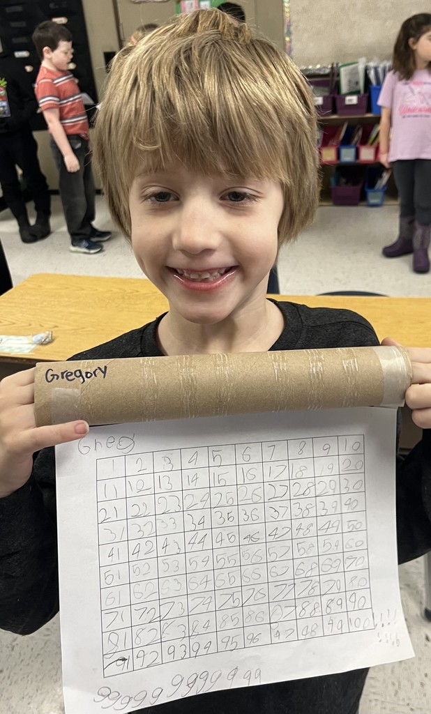 A blonde boy grins widely while holding his chart. At the bottom of his paper, he has playfully written a long string of the number 9.