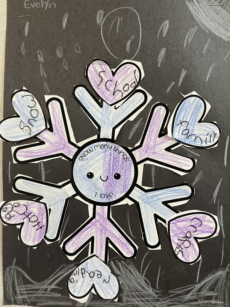 ) A close-up of a student art project titled "SNOW many things I love" by a student . It features a hand-colored purple and light blue snowflake on black paper. Six paper hearts are attached to the points of the snowflake, each containing a word: School, Family, Crafts, Reading, Hot cocoa, and Snow. White crayon marks on the background represent falling snow.  