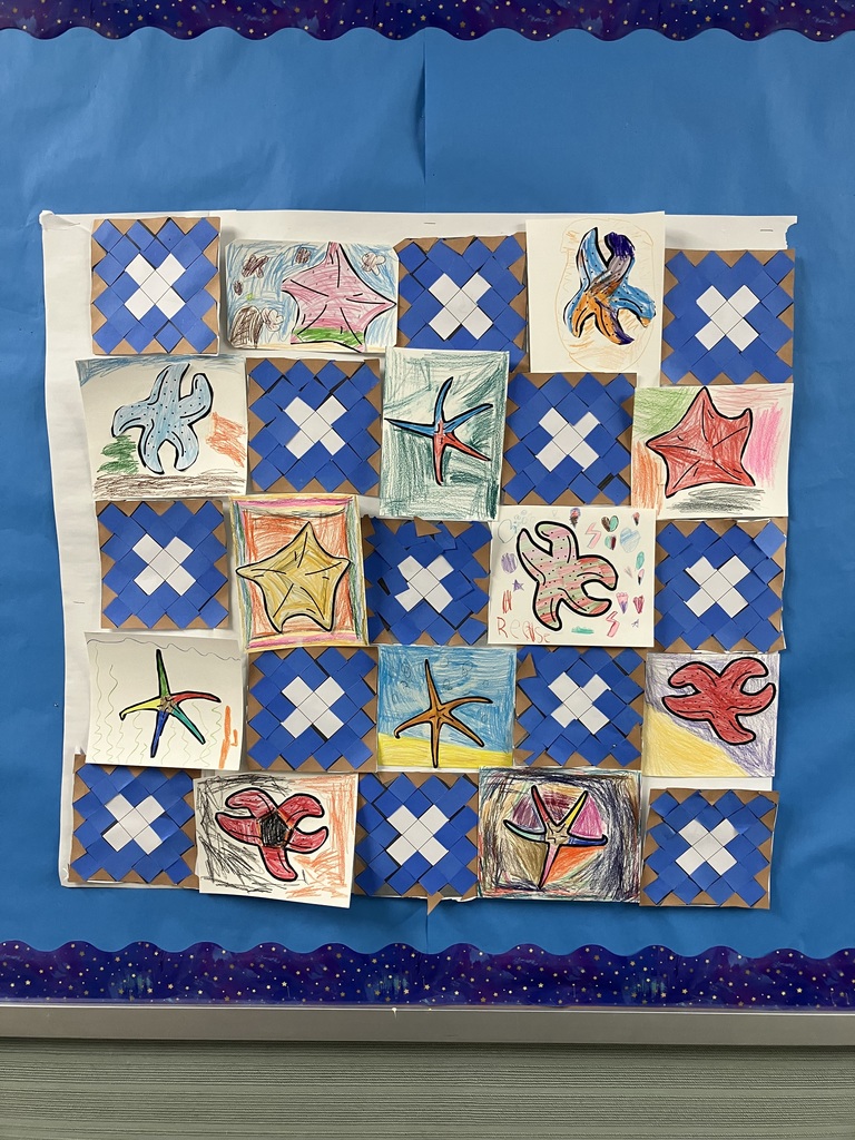 A bulletin board displays a grid of children's artwork. It features alternating squares of blue and white woven paper mats and colorful crayon drawings of starfish in various shapes and colors. The display is mounted on a large sheet of white paper against a blue background with a starry border. 