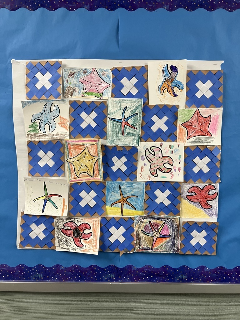 A bulletin board displays a grid of children's artwork. It features alternating squares of blue and white woven paper mats and colorful crayon drawings of starfish in various shapes and colors. The display is mounted on a large sheet of white paper against a blue background with a starry border. 