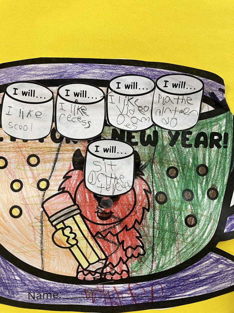  A close-up of a student’s New Year's craft The paper mug is colored with green, orange, and purple crayons, featuring a red cartoon yeti holding a large pencil. Five paper marshmallows are glued to the top of the mug with handwritten goals: "I like scool," "I like recess," "I like Video games," "Pla the ninten do," and "Sit on the tere." 
