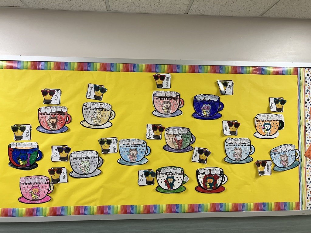 Classroom Bulletin Board  Alt Text: A classroom bulletin board with a bright yellow background and a colorful rainbow-striped border. The board is decorated with numerous student art projects featuring the pun "YETI FOR A NEW YEAR!" Each project consists of a paper mug cutout containing a cartoon yeti holding a pencil. Above each mug is a paper lightbulb featuring a student’s name and a pair of sunglasses. The mugs are colored in various shades, and small paper "marshmallows" with handwritten resolutions are glued to the top of each mug. 