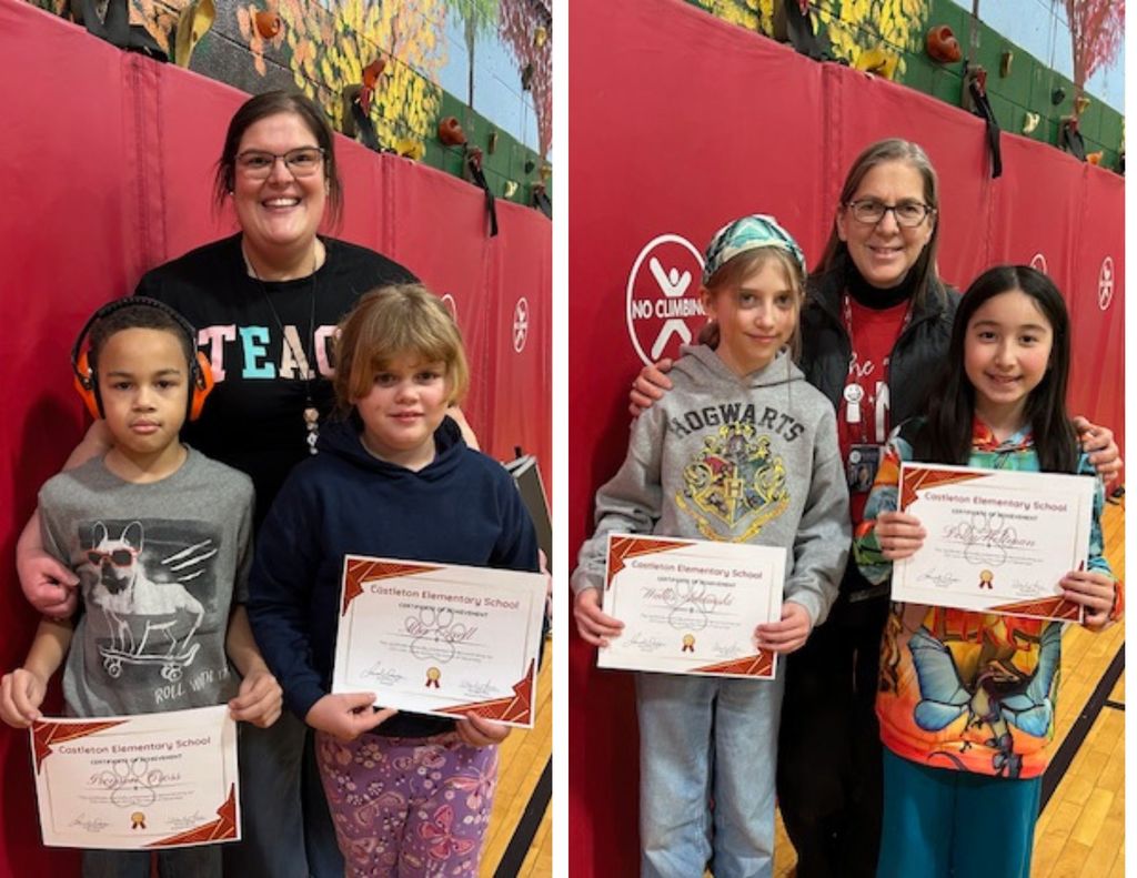 Two students display certificates while standing beside a staff member in a school gym, posed in front of red padding.