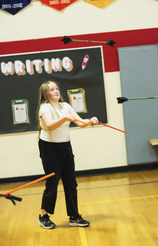 Student tossing and catching juggling clubs while practicing coordination during the circus workshop.