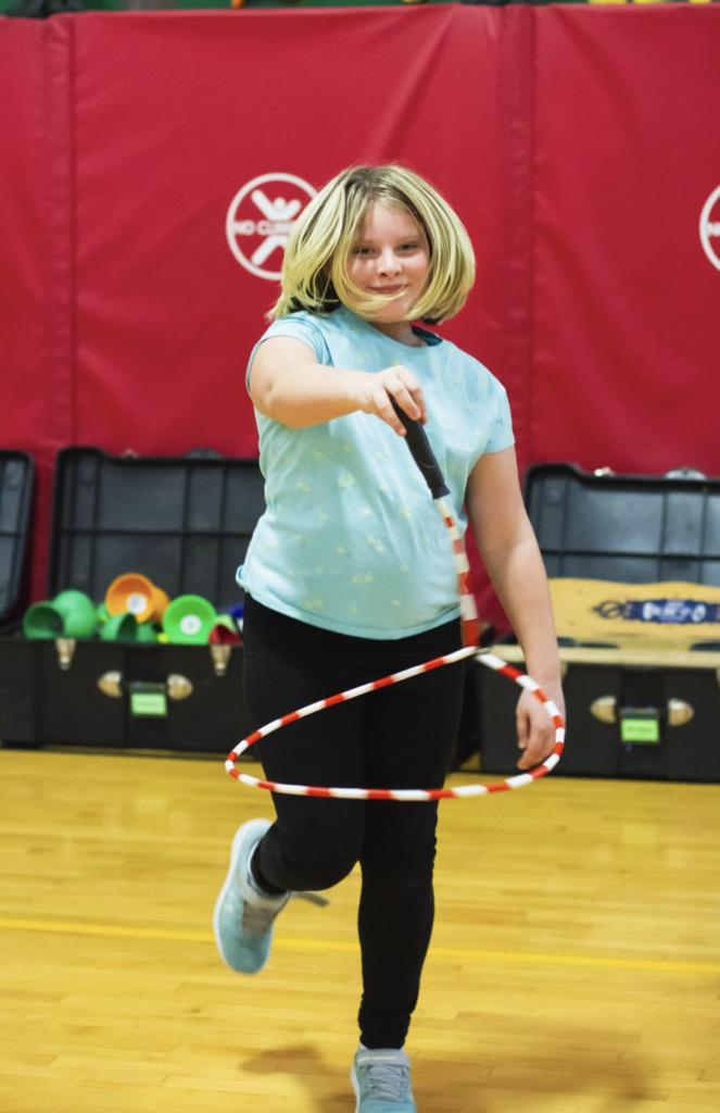 Student hula-hooping while walking across the gym floor during the circus workshop.