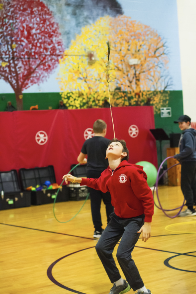 Student balancing a feather on their face while standing in the gym during a circus challenge.