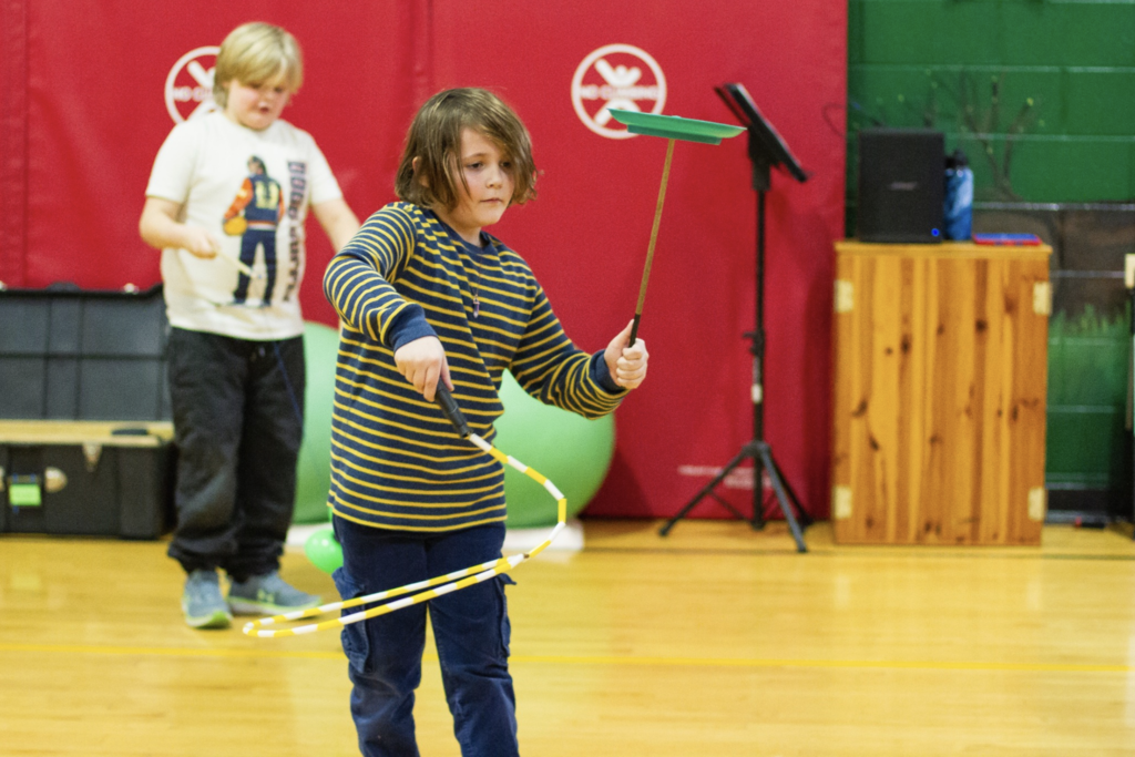 Student spinning a plate on a stick with focused expression during the circus skills session.