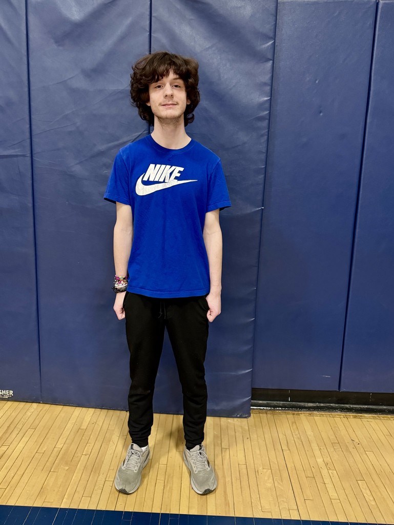 A student stands in the gym holding equipment, assisting with stage and setup changes between talent show acts.