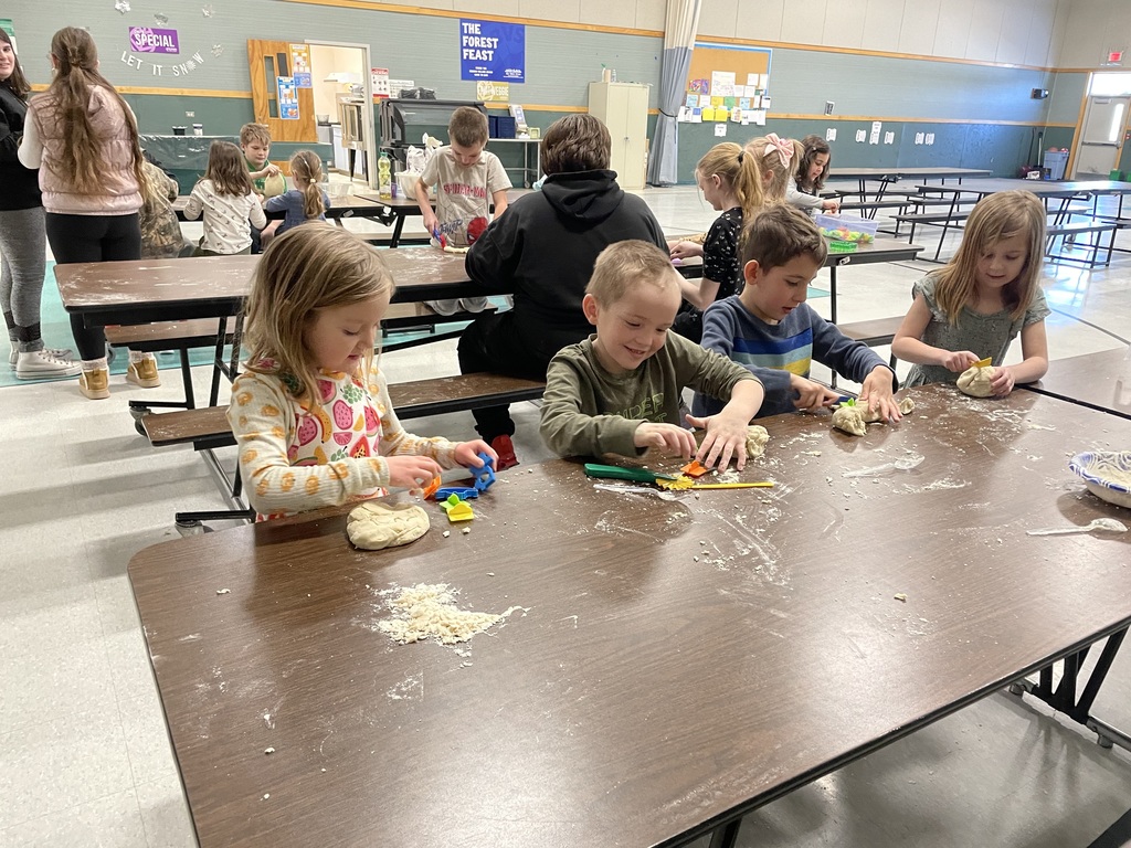 This second image offers another perspective of the group activity, showing several more children focused on their dough creations at the long cafeteria tables.