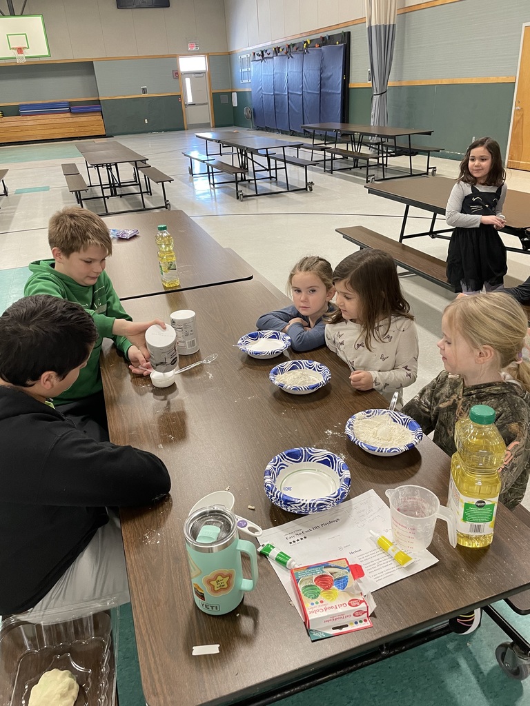 These images capture children participating in a hands-on playdough making activity within a school cafeteria or gymnasium.