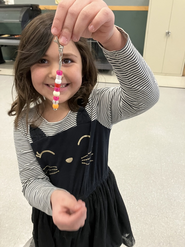 A young girl in a cat-themed dress smiles while displaying a finished bead keychain