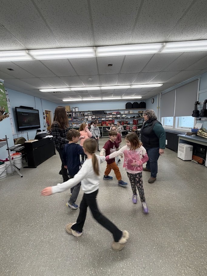 Students walk and dance in a circle during a music and movement activity in a classroom filled with instruments.