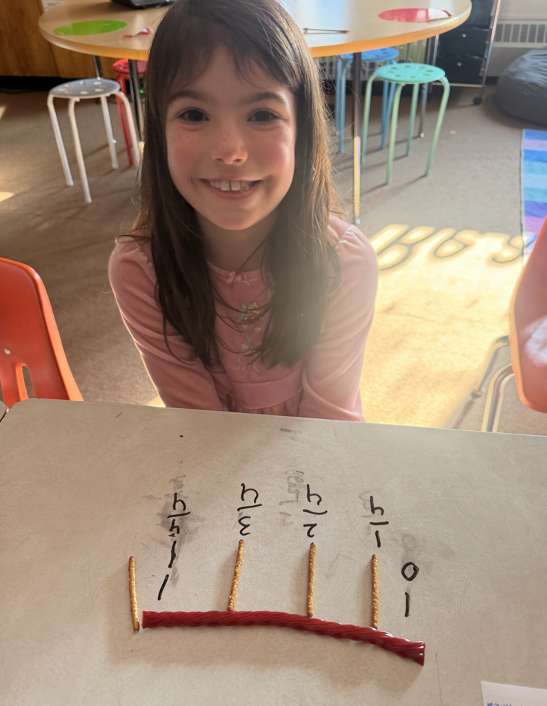 Student sits at a desk labeling fractions on a number line created with pretzel sticks and licorice.