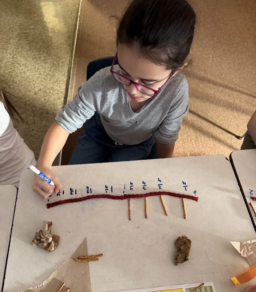 Student wearing glasses writes fraction labels on a pretzel-and-licorice number line during a hands-on math activity.