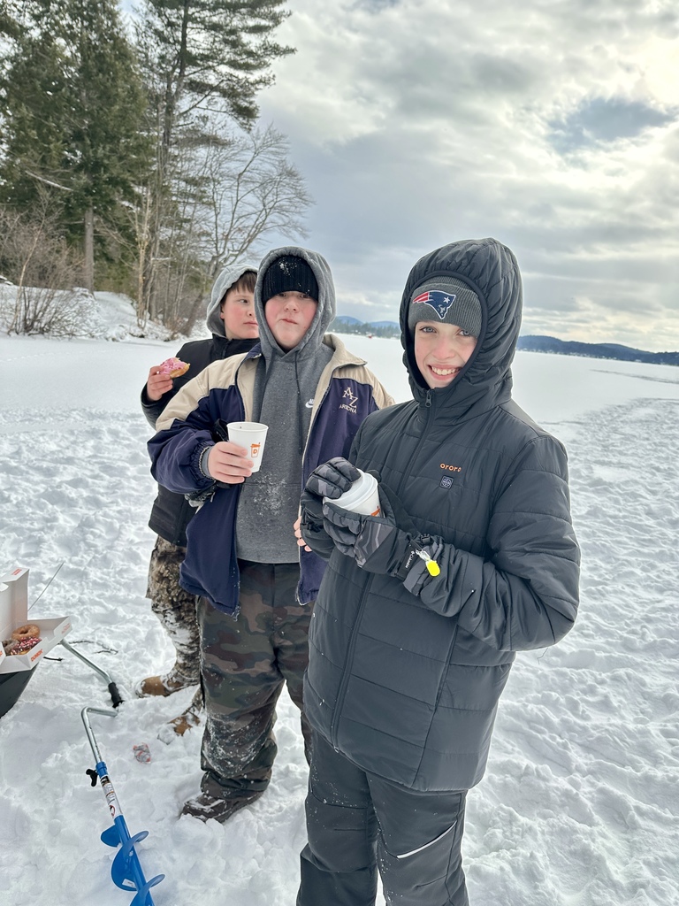Three bundled-up students stand on the ice holding hot drinks and a donut, with a frozen lake and trees in the background.