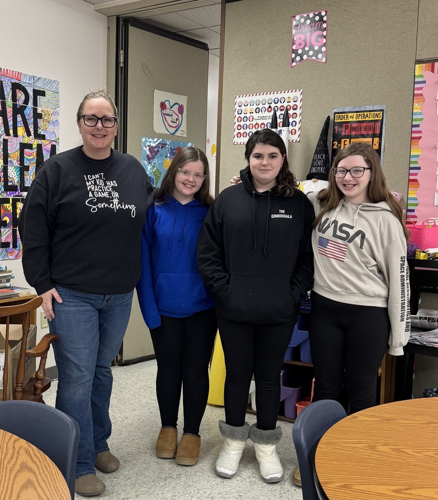 An adult woman and three young girls pose for a group photo in a classroom setting.