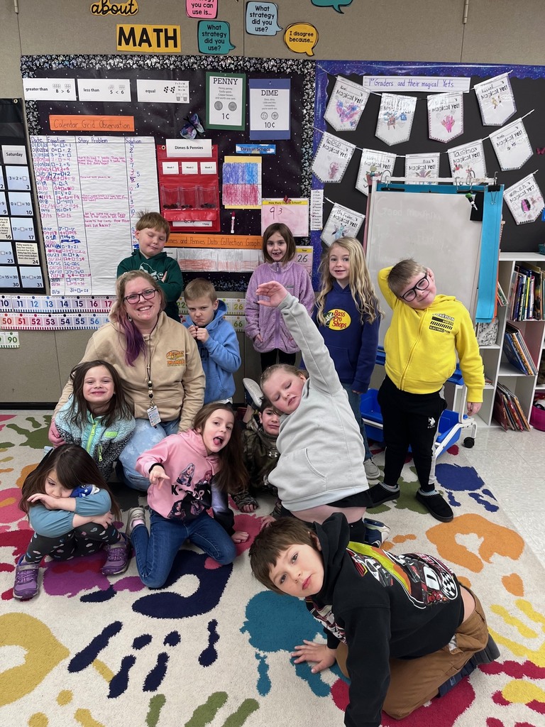 In this image, a group of ten children and one adult are posing together in a classroom setting.
