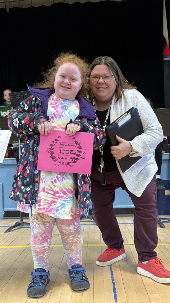 Student and adult smile for the camera; the student holds a pink certificate while the adult holds a folder.