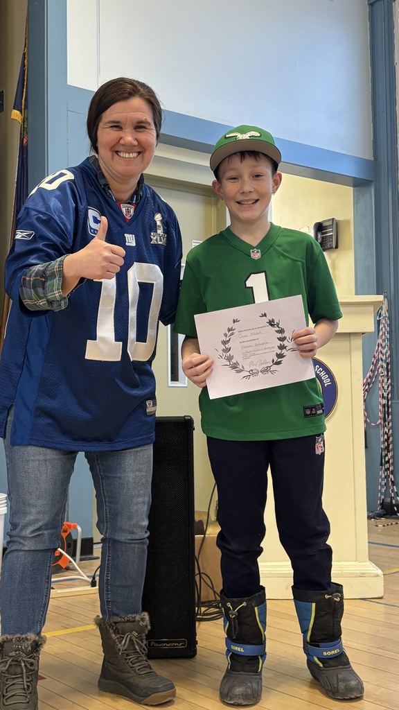 Adult and student pose side by side indoors, both smiling; the student holds a printed certificate while the adult gives a thumbs-up.