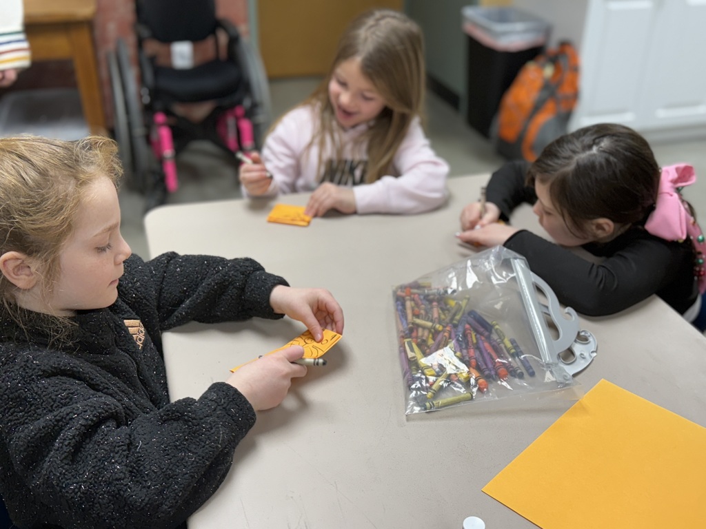 Three children work on small art cards with crayons and markers during a story time craft activity.
