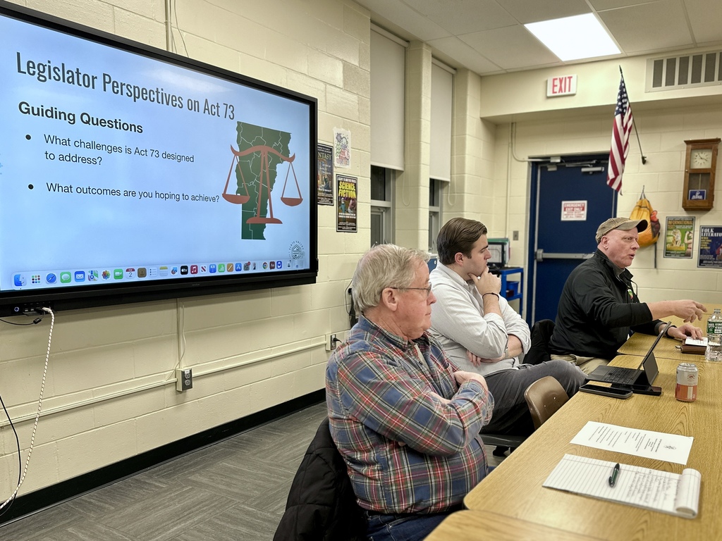 Three local legislators speak at a table during a community forum, with a display screen behind them reading “Legislator Perspectives on Act 73” and listing guiding questions.